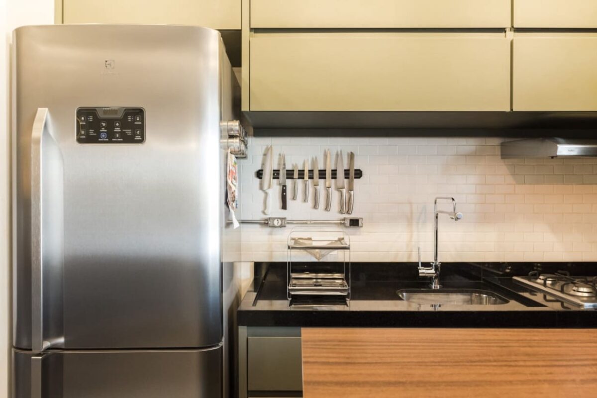 Geladeira, talheres na parede e um armário com cooktop e pia em uma cozinha