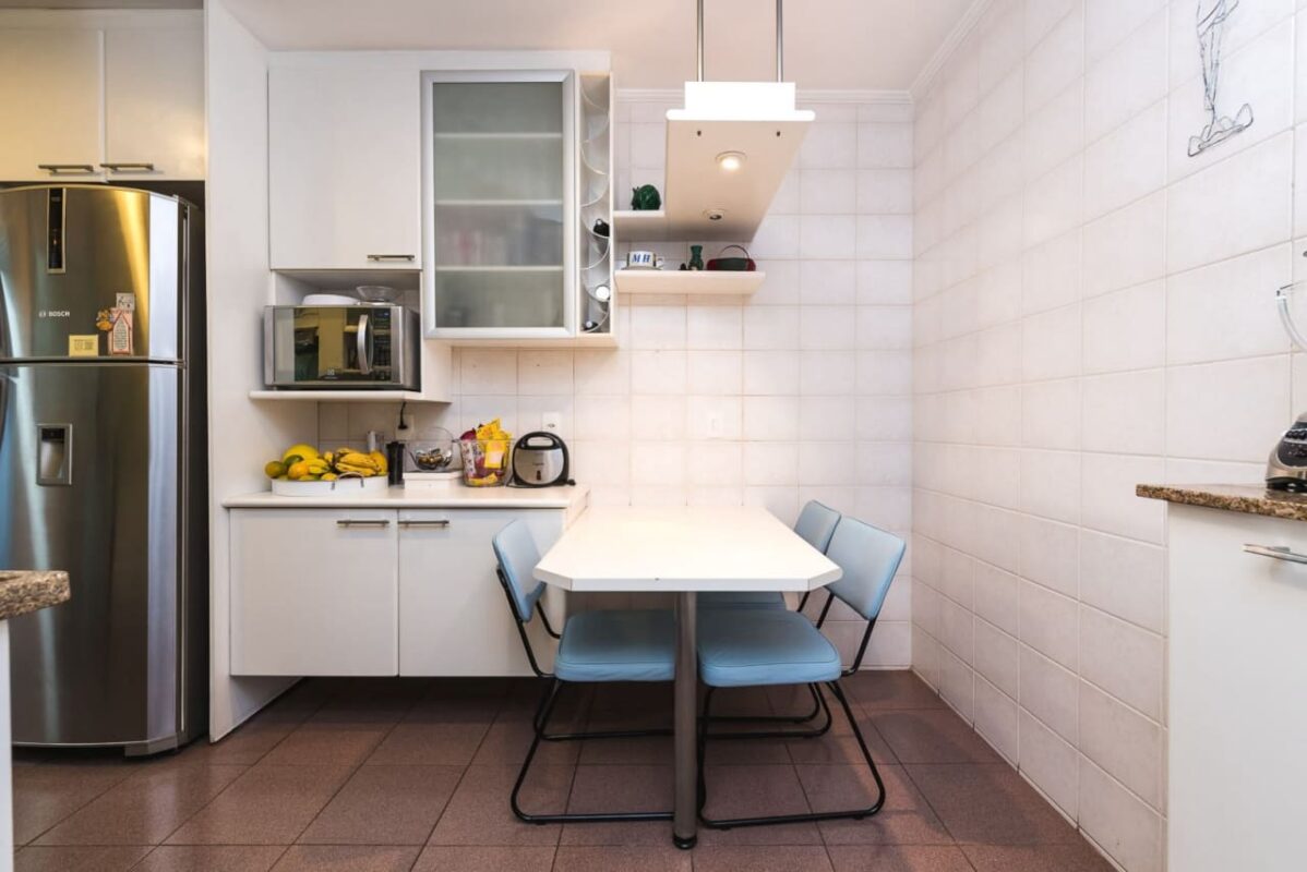 Cozinha compacta com móveis, eletrodomésticos modernos e uma luminária pendente no teto sobre a mesa de jantar