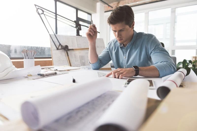 Um homem profissional trabalha em um projeto em uma mesa com lápis e papéis